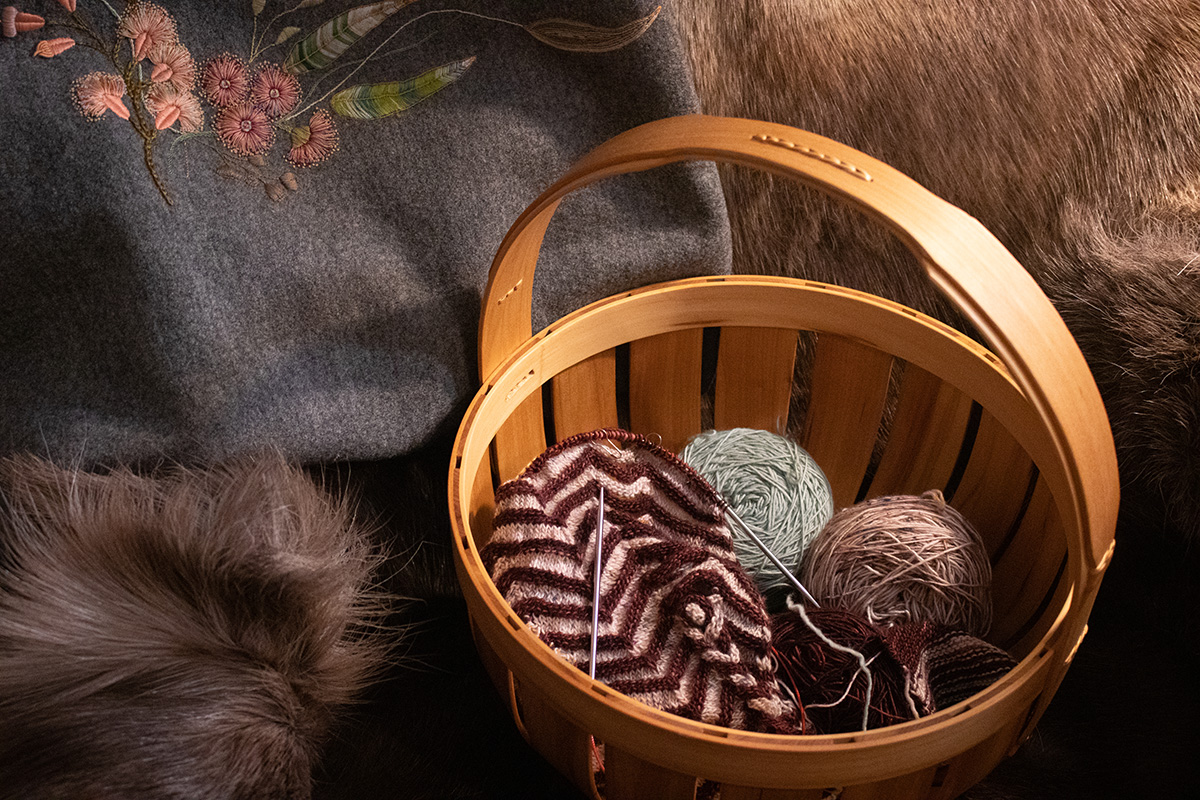 An image of a brown basket with in-progress knitting in pink and grey yarn